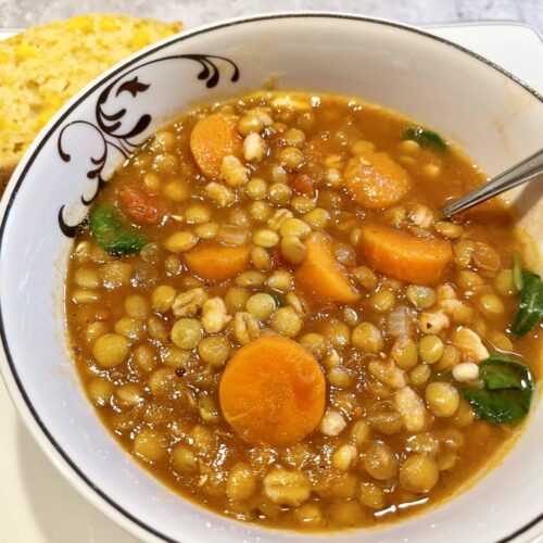 Carrot and lentil soup in a white bowl with a decorative swirl next to a piece cornbread.