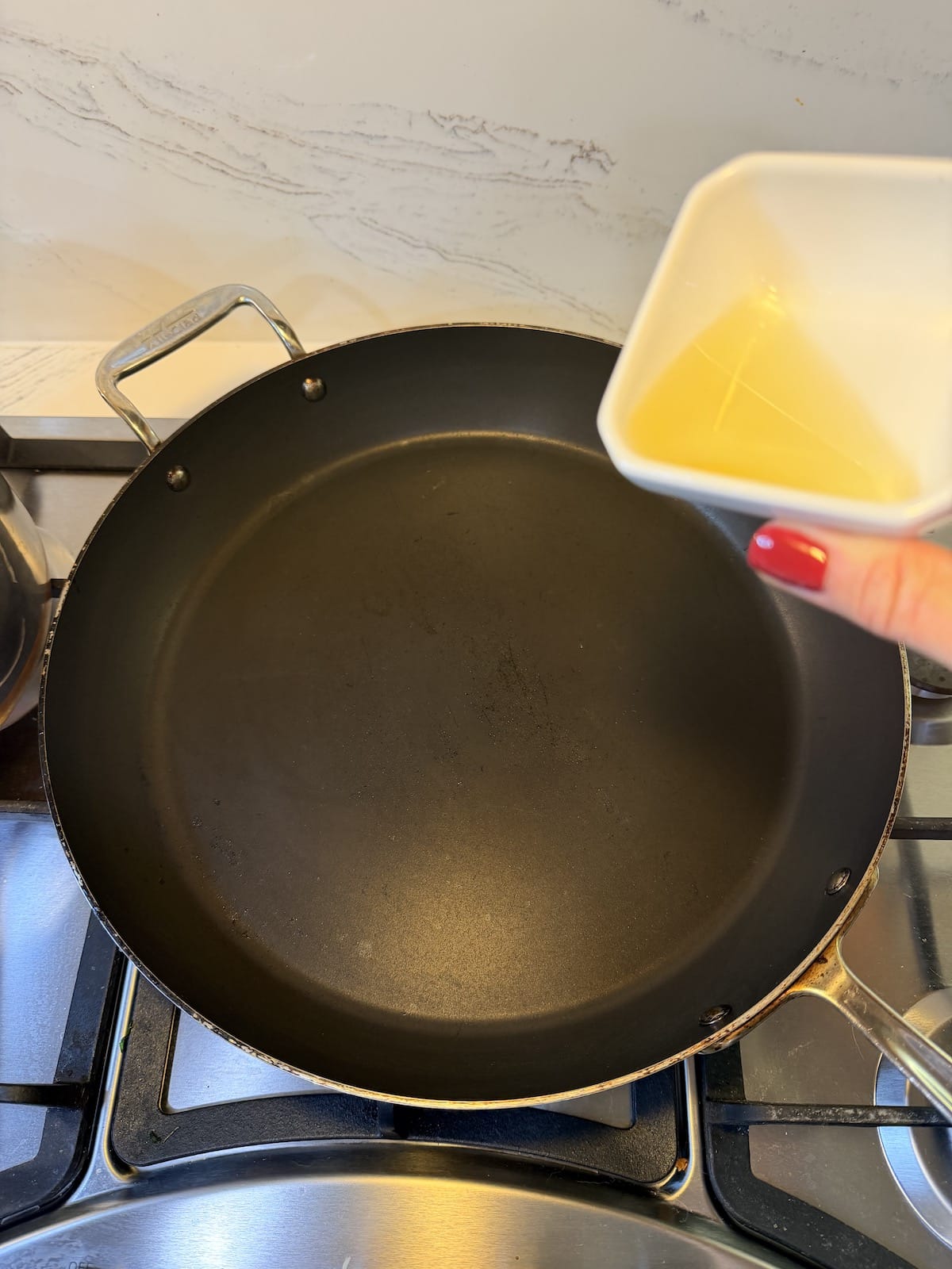 Olive oil in a white ramekin that is going to be pour into a saucepan over the stovetop.