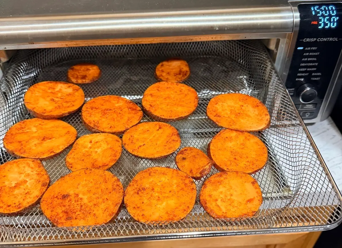 Seasoned sweet potato slices in the air fryer basket ready to be cooked.
