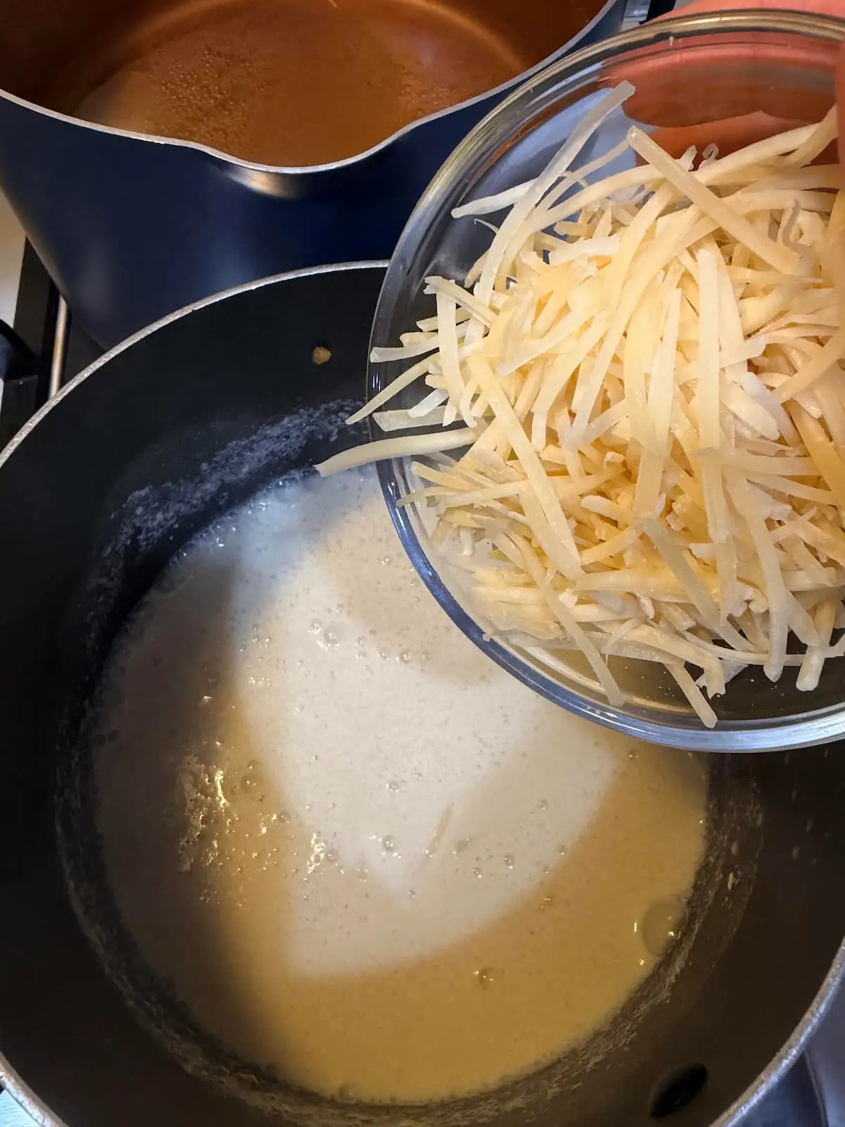 Adding shredded parmesan cheese to a sauce pan with a creamy sauce.