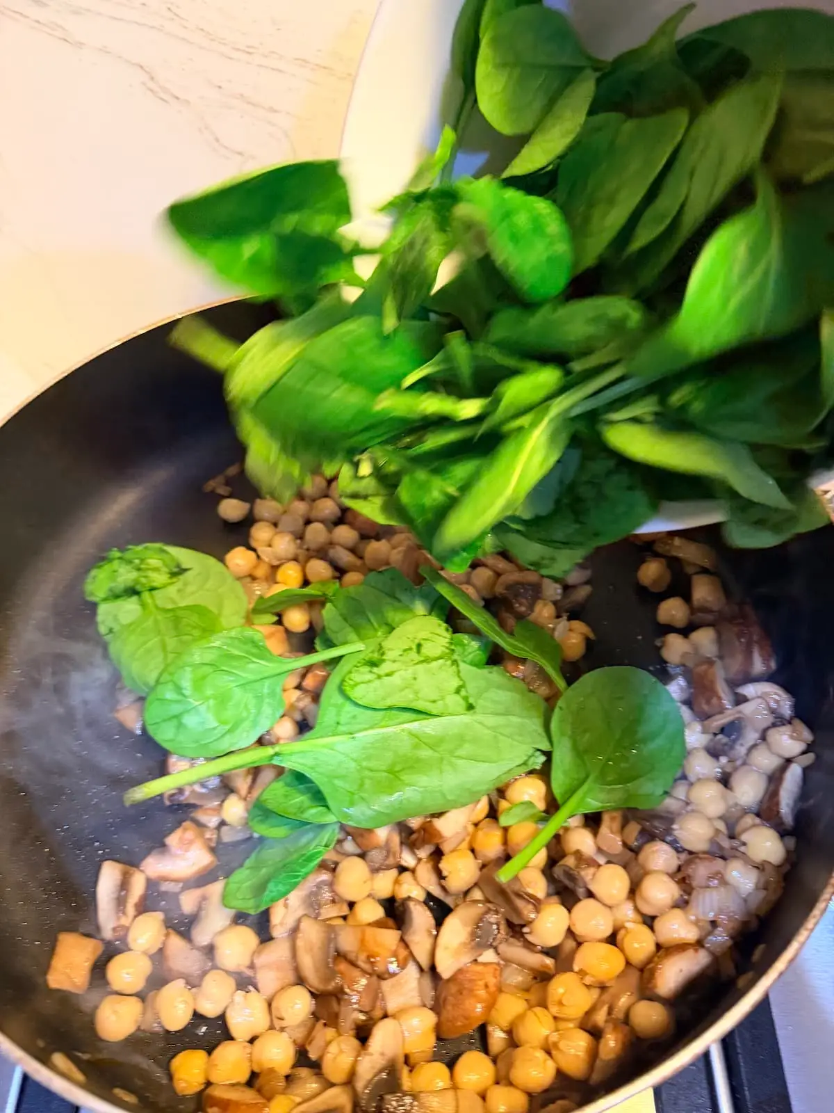 Adding raw baby spinch to a skillet with shallots, mushrooms, and garbanzo beans.