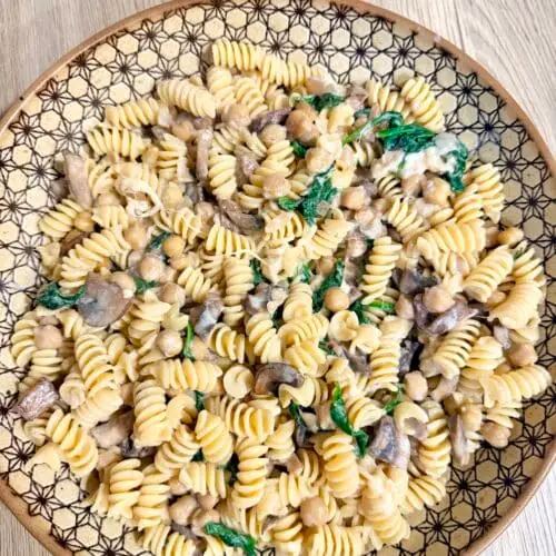 Creamy vegetarian pasta in a large serving bowl atop a wooden surface.