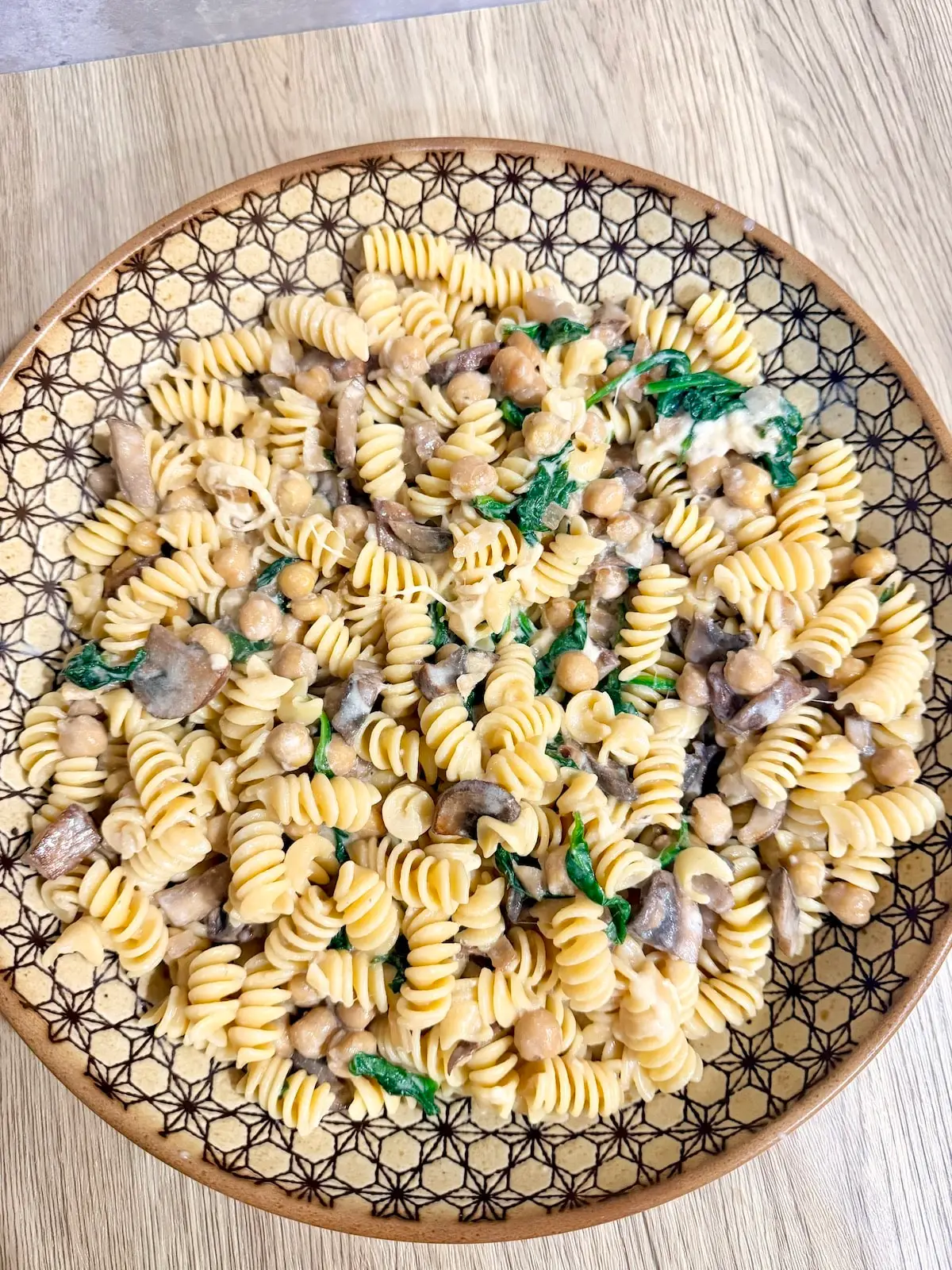 Creamy vegetarian pasta in a large serving bowl atop a wooden surface.