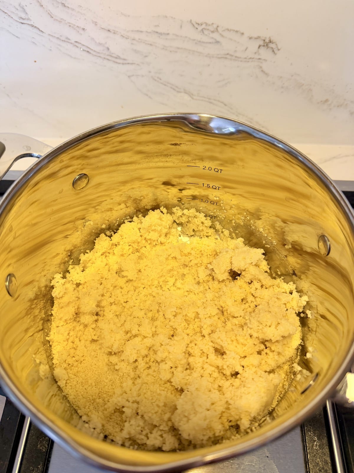 Cooked couscous in a silver pot atop a stovetop.