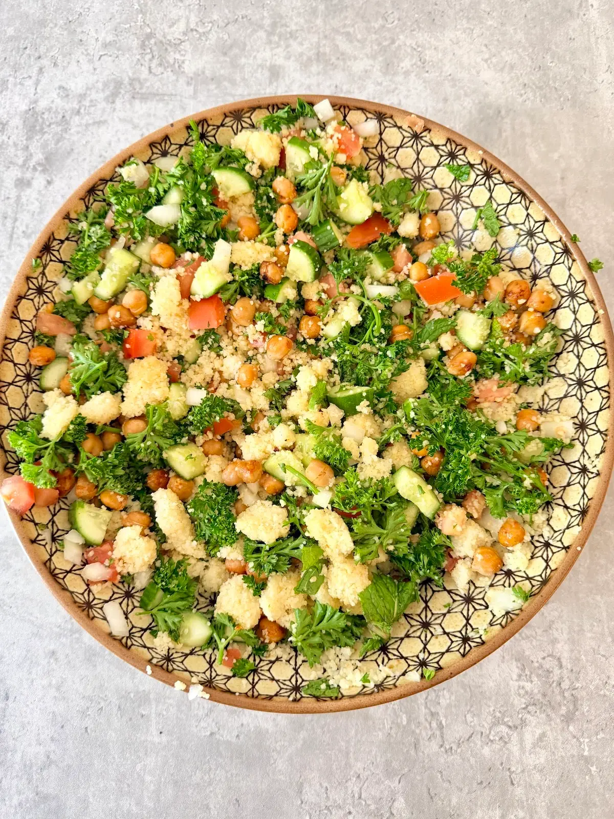 Tabbouleh couscous salad in a large patterned bowl atop gray surface.