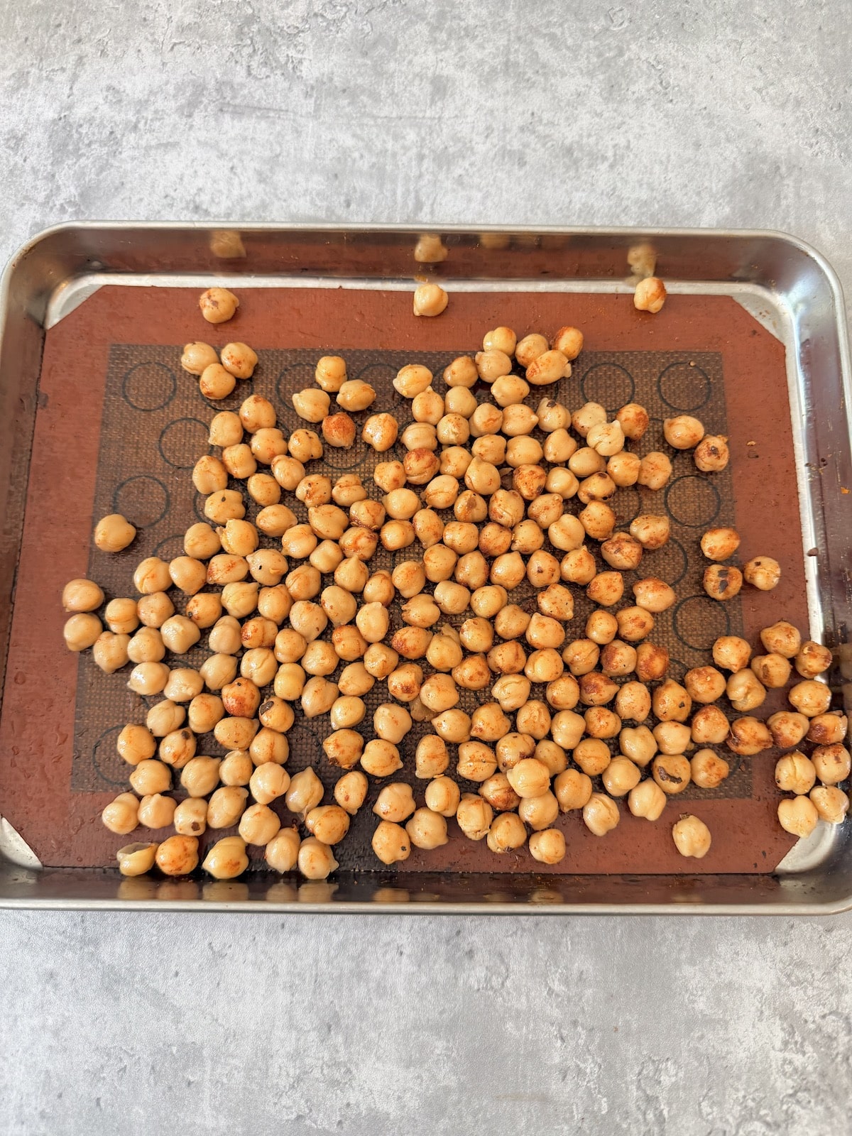 Chickpeas that are seasoned with smoked  paprika, child flakes, and black pepper atop a silicon lined baked sheet.