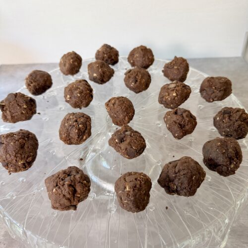 Date Protein Balls with Peanut Butter and Chocolate atop a crystal serving platter that is on a gray surface.