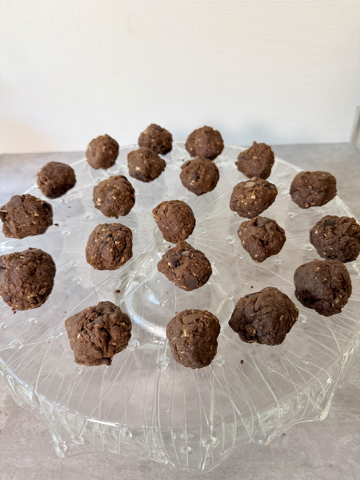 Date Protein Balls with Peanut Butter and Chocolate atop a crystal serving platter that is on a gray surface.