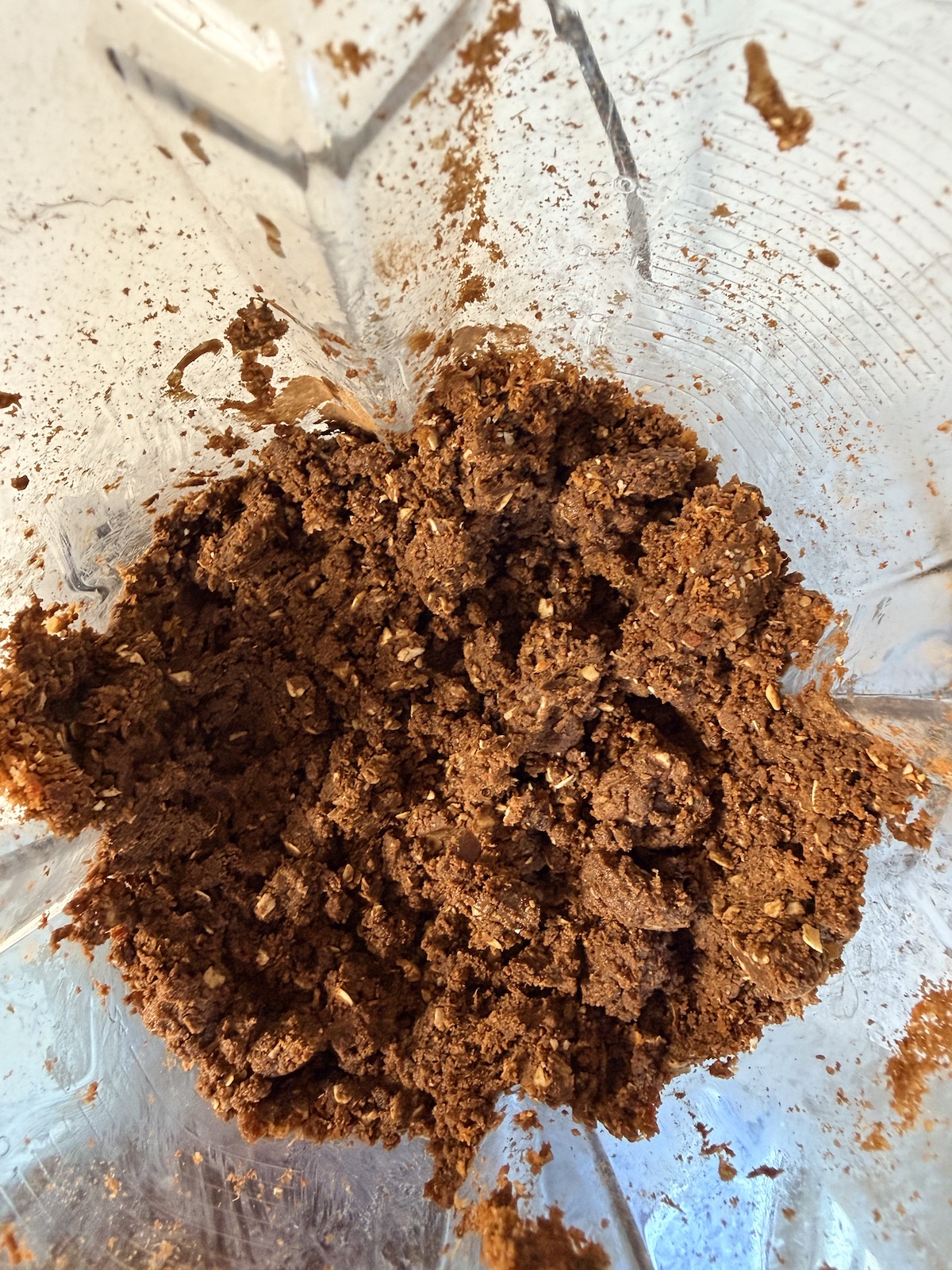 A blender container with the crumbly texture of the date protein balls with peanut butter & chocolate after it has been blended.
