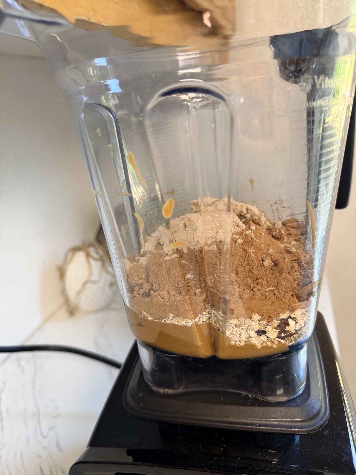 Medjool dates, cocoa powder, protein powder, peanut butter, oats, and vanilla extract in a blender container.