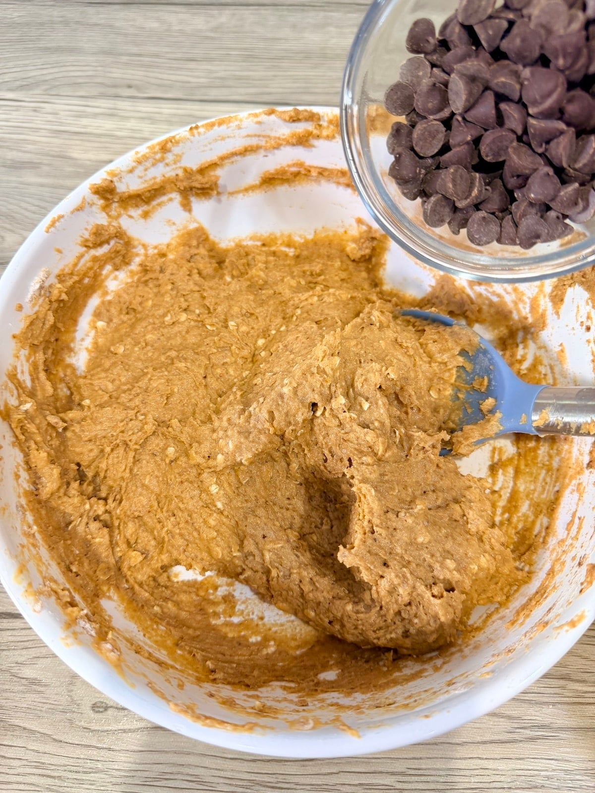 In a large white mixing bowl, adding the chocolate chips to the healthy pumpkin muffin batter.