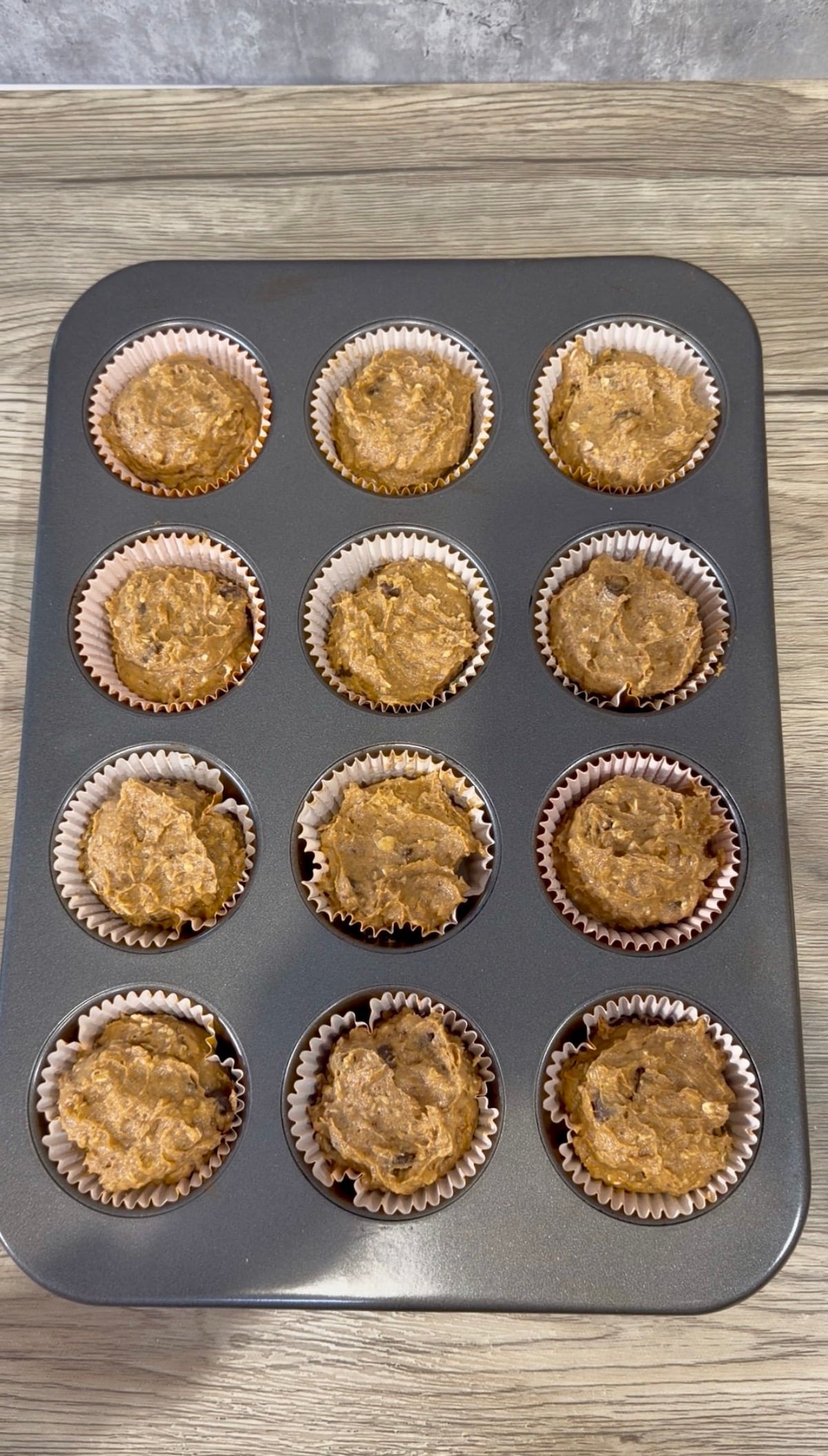 Healthy pumpkin muffin batter in muffin tin lined with muffin cups atop a wooden surface.