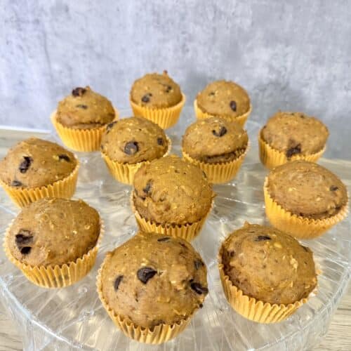 Healthy pumpkin muffins in orange muffin cups atop a crystal stand that is on top of a wood surface.