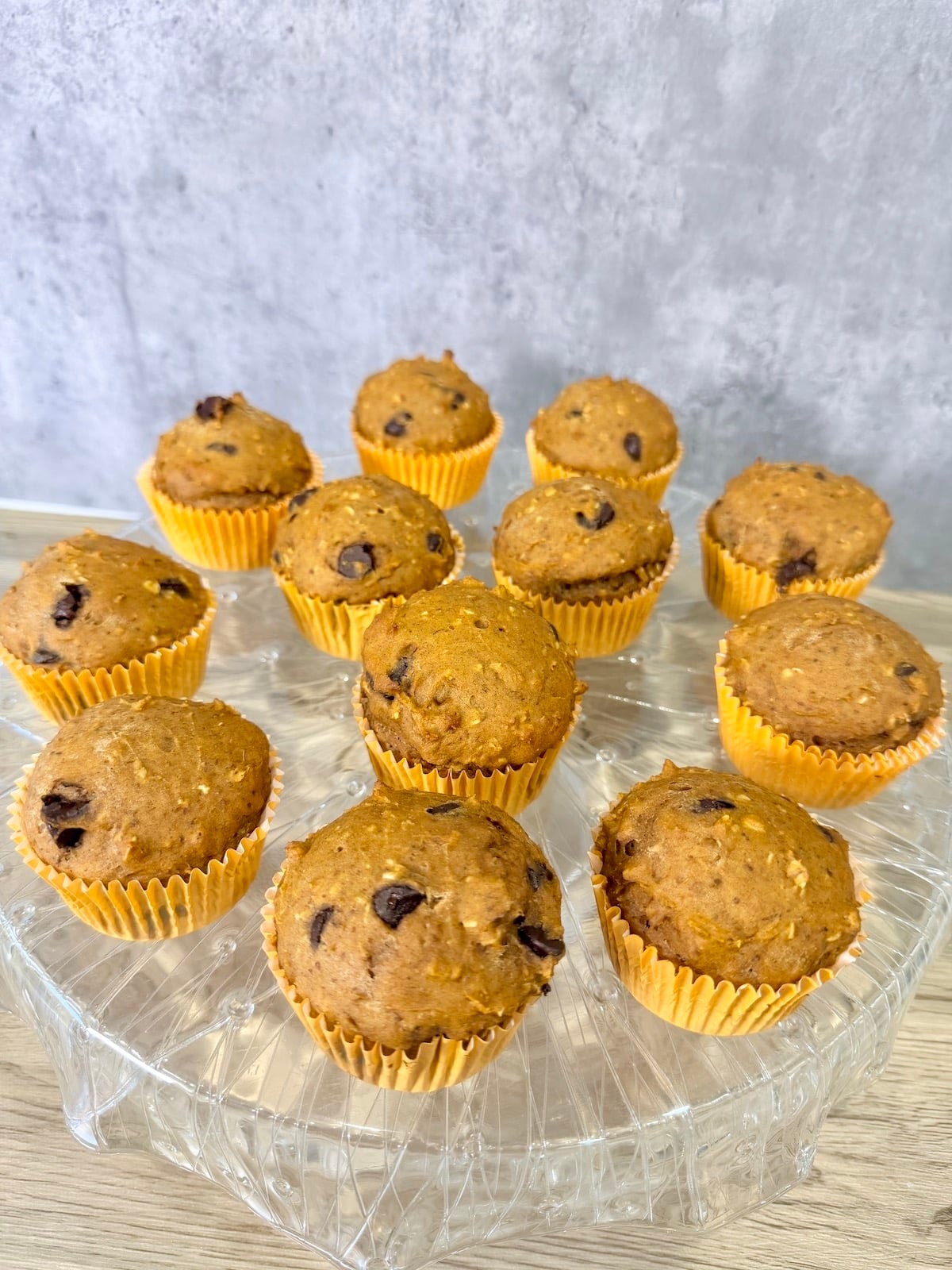 Healthy pumpkin muffins in orange muffin cups atop a crystal stand that is on top of a wood surface.