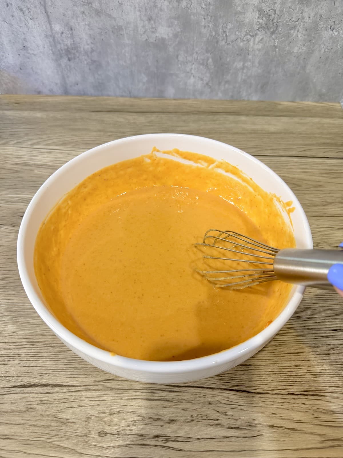 A large white mixing bowl with healthy pumpkin muffin batter atop a wooden surface.